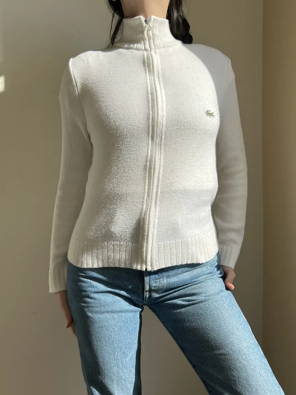 Sweater blanco con cierre y cuello alto de la marca Lacoste. Ideal para un look casual y abrigado.