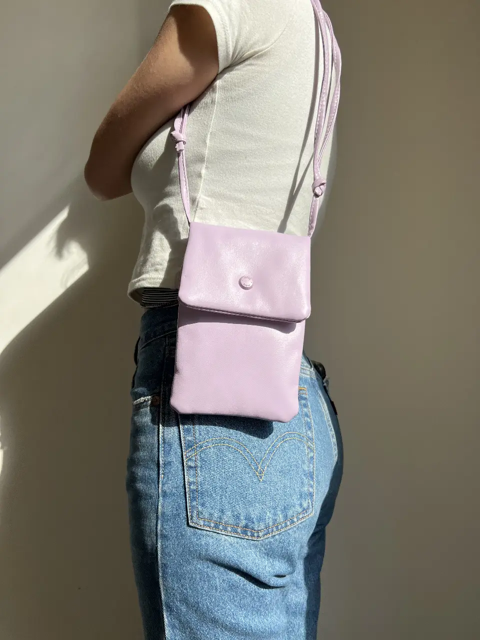 Bandolera de cuero sintético color lila, con solapa y botón a presión. Ideal para llevar lo esencial con estilo.