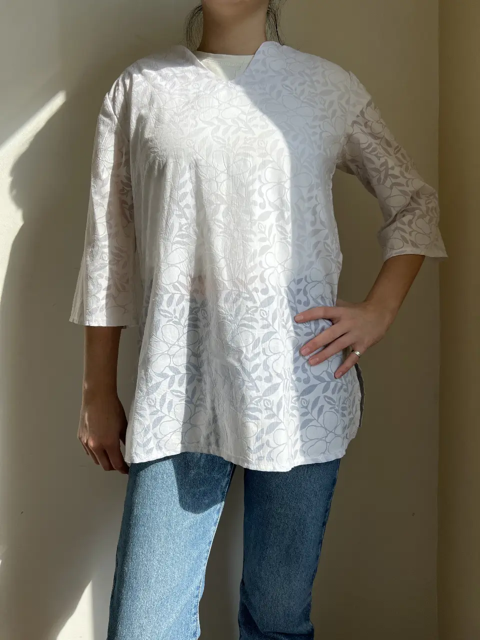 Blusa blanca con estampado floral en relieve, mangas 3/4 y cuello en V. Ideal para un look casual y fresco.