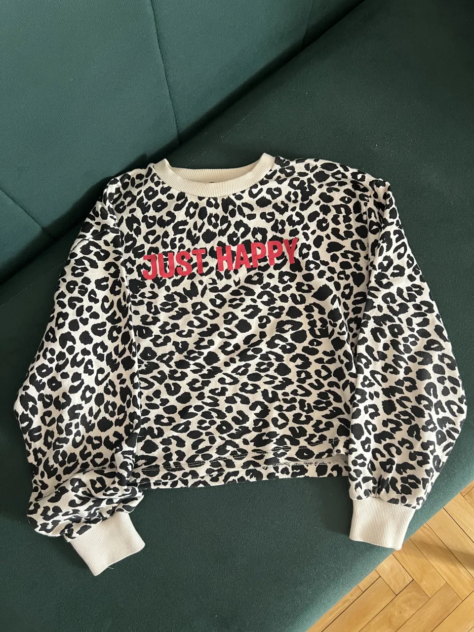 Buzo de algodón con estampa de leopardo en blanco y negro. Tiene la frase "JUST HAPPY" en color rojo en la parte delantera. Puños y cuello redondo en color crudo.