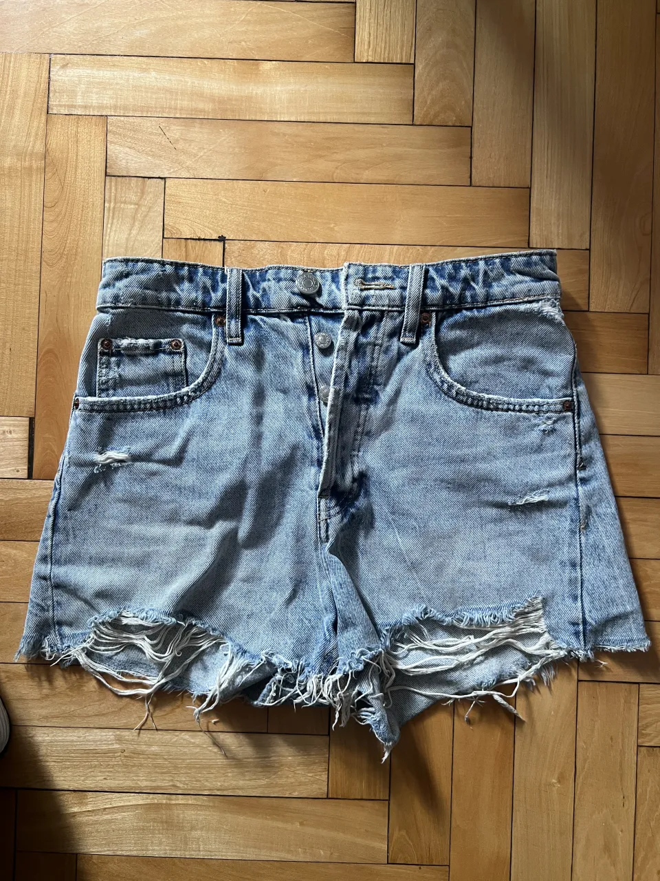 Shorts de jean tiro alto con roturas y detalles deshilachados en el borde inferior. Posee bolsillos delanteros y traseros.