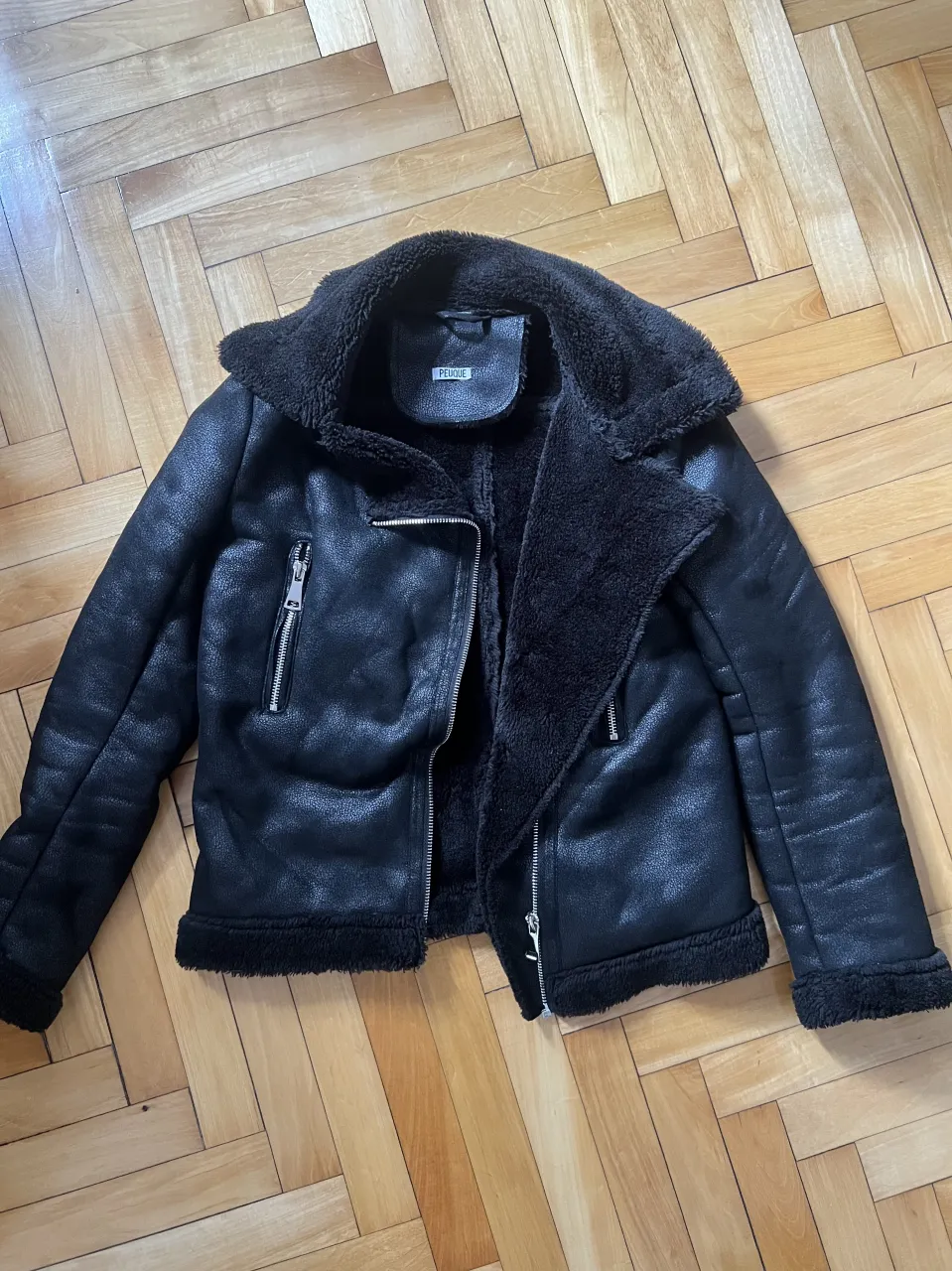 Campera negra de cuero sintético con cuello y forro de corderito. Cierre frontal y bolsillos con cierre.