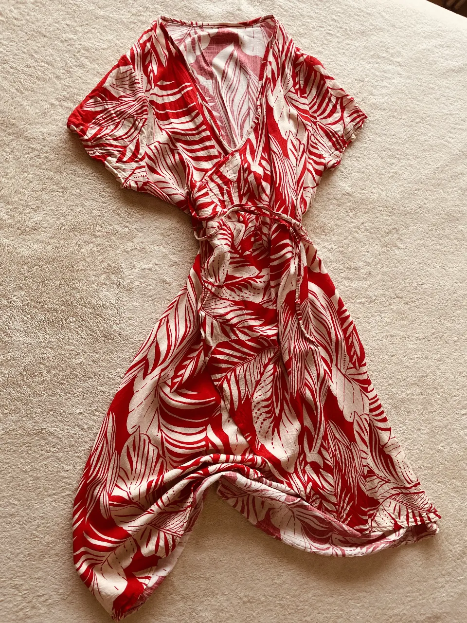 Vestido corto estampado con hojas en rojo y blanco. Diseño cruzado con mangas cortas y cintura ajustable con lazo. Ideal para un look fresco y playero.