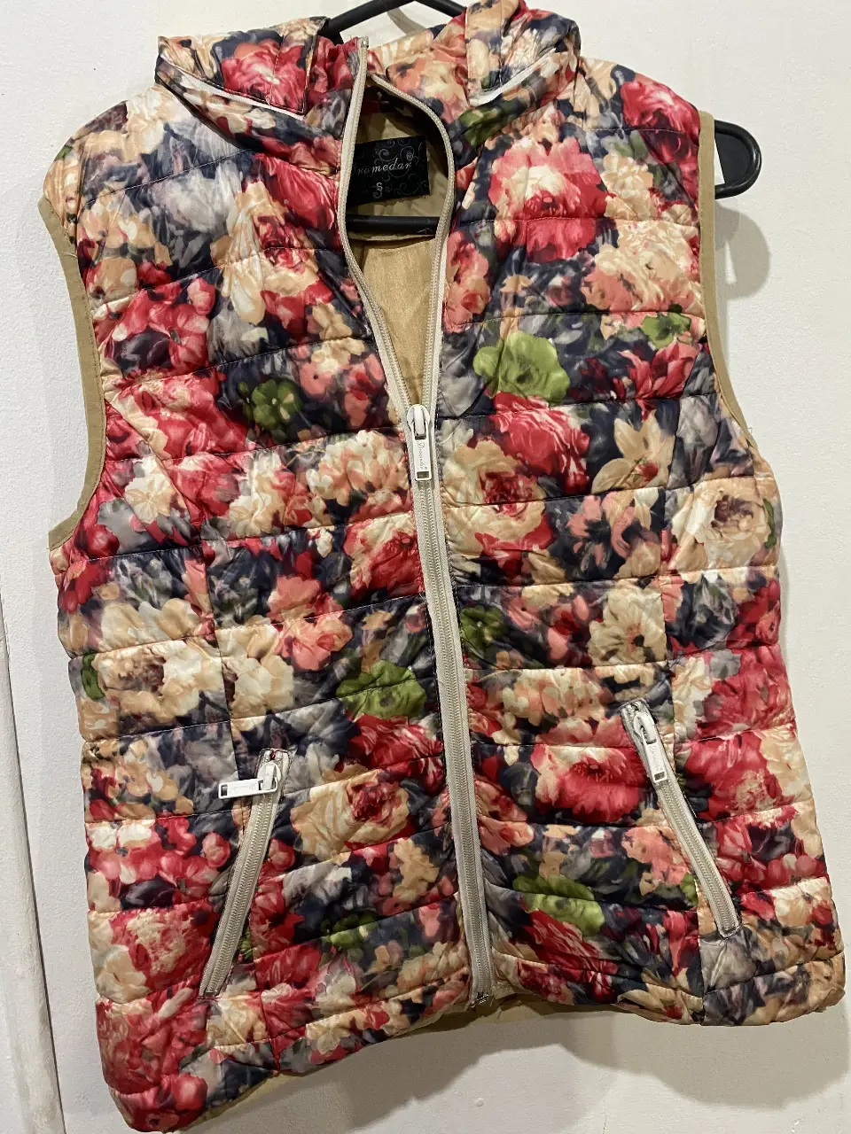 Chaleco acolchado con capucha y estampado floral. Ideal para sumar abrigo y estilo a tus looks de entretiempo. Cuenta con cierre y bolsillos.