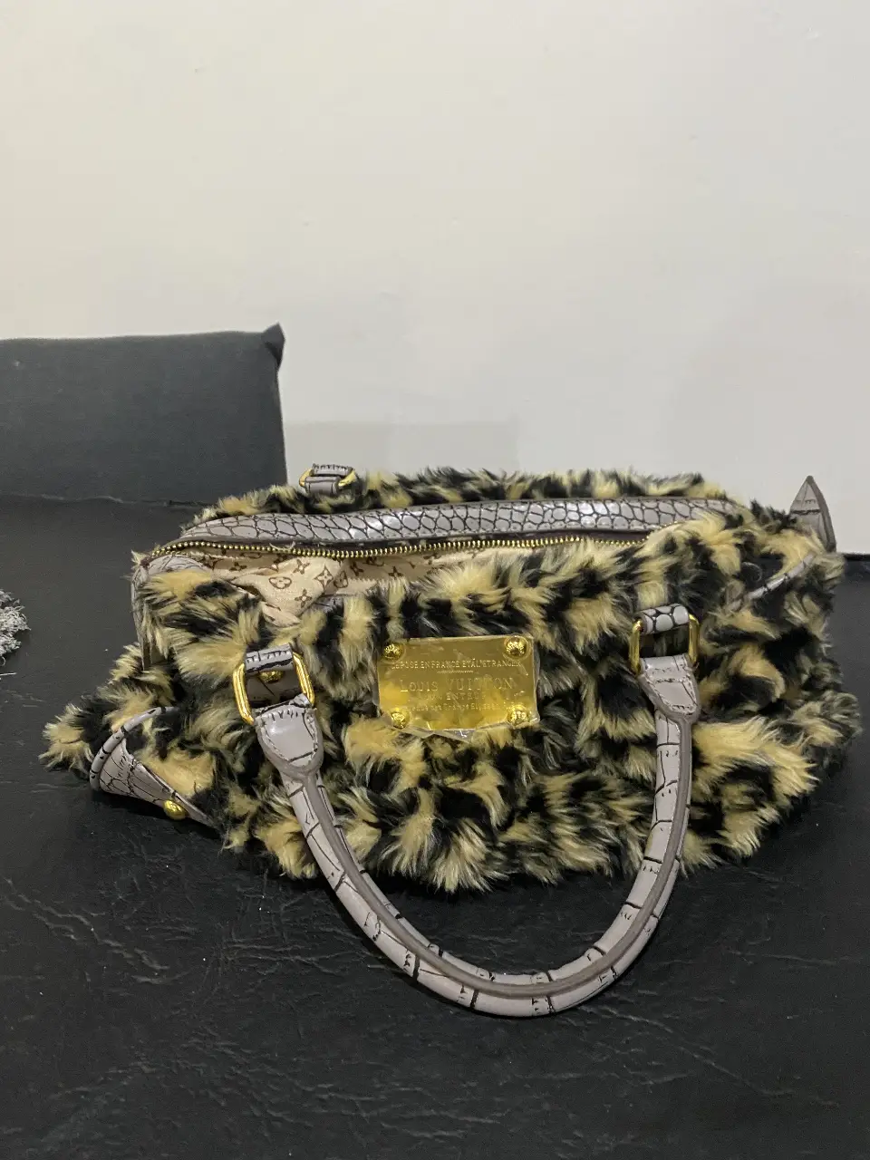 Cartera de mano con estampado de leopardo y detalles en gris. Confeccionada con un material similar a la piel, esta cartera de diseño único es ideal para darle un toque audaz a cualquier look. Cuenta con un cierre y un interior forrado con el monograma de la marca.