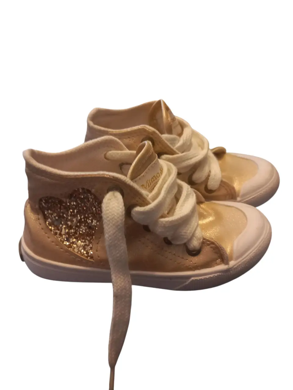 Zapatillas doradas para niña, con detalle de corazón con brillos y cordones blancos. Ideales para un look casual y cómodo.
