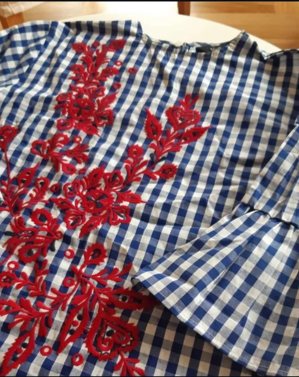 Blusa de mujer a cuadros azul y blanco con bordado floral rojo en el frente. Manga larga con volados.