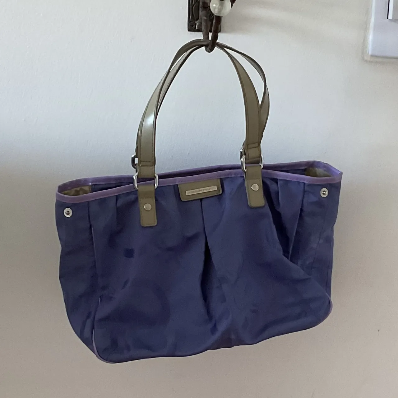 Bolso tote de tela color azul Francia, con manijas de cuero sintético color verde militar. Interior forrado en tela color crudo y detalles en violeta. Cierre superior con broches.