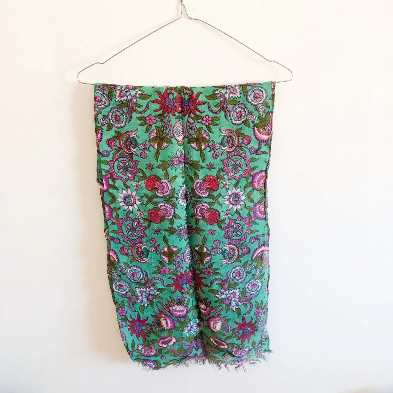Pañuelo de tela con estampado floral en tonos verdes, rosas y violetas. Ideal para complementar cualquier look con un toque bohemio y artesanal.