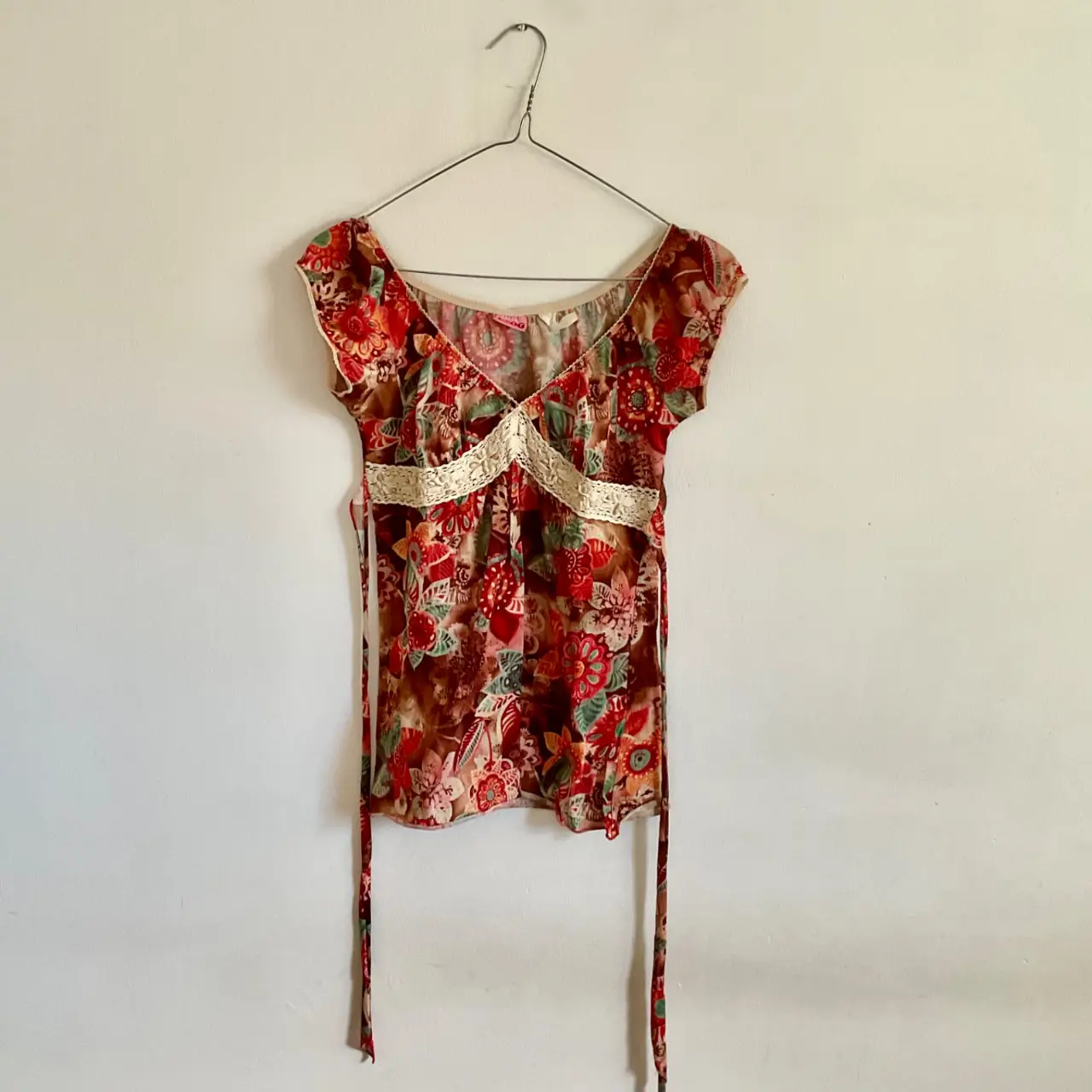 Blusa vintage con estampado floral en tonos rojos y marrones, detalles de encaje en el escote y la cintura. Ideal para un look bohemio y femenino.