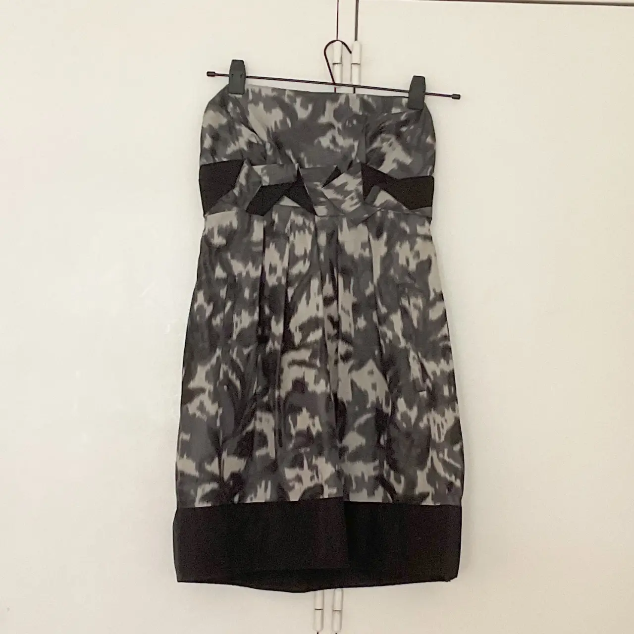 Vestido strapless con estampado abstracto en tonos grises y negros. Detalles de lazo en la cintura y borde inferior negro. Ideal para eventos formales o fiestas.