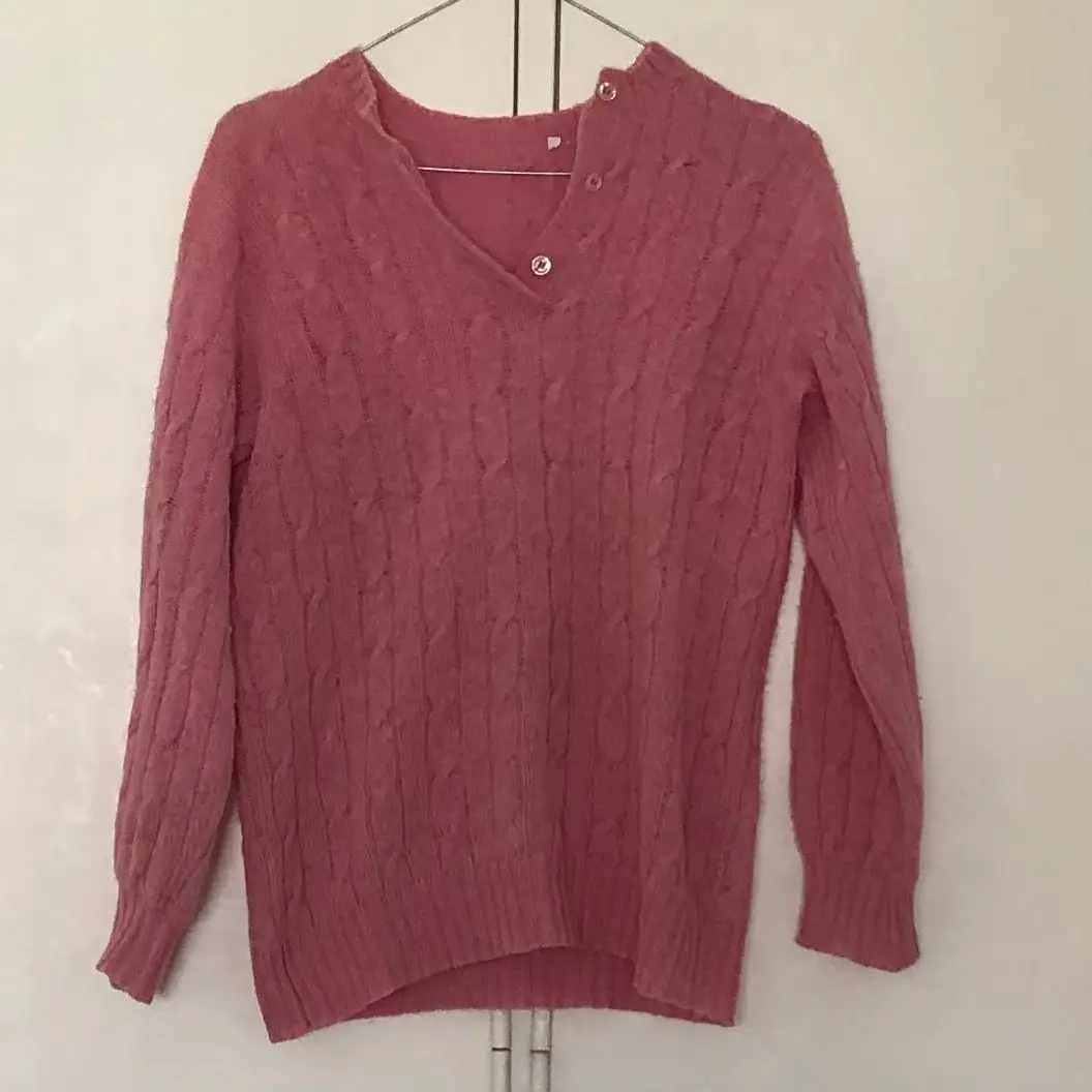 Sweater rosa de punto con diseño de trenzas, cuello en V y botones decorativos. Ideal para un look casual y abrigado.