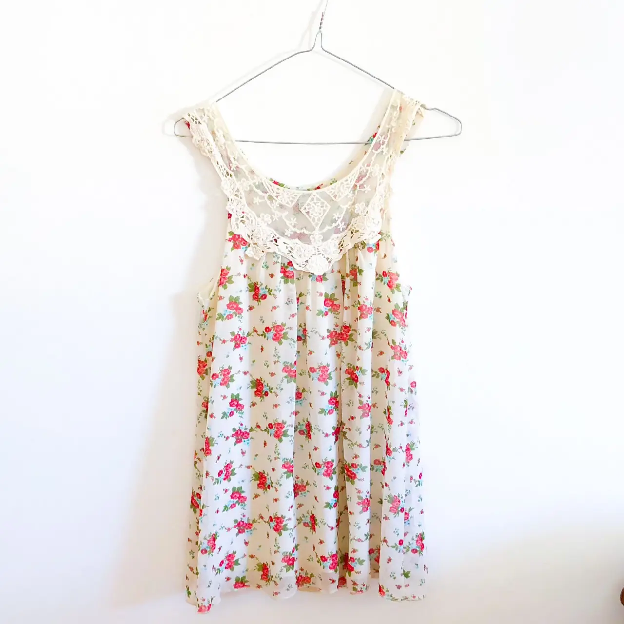 Vestido mini de mujer, con estampado floral en tonos rojos y blancos. Presenta un detalle de encaje en la parte superior y tirantes finos. Ideal para un look fresco y romántico.