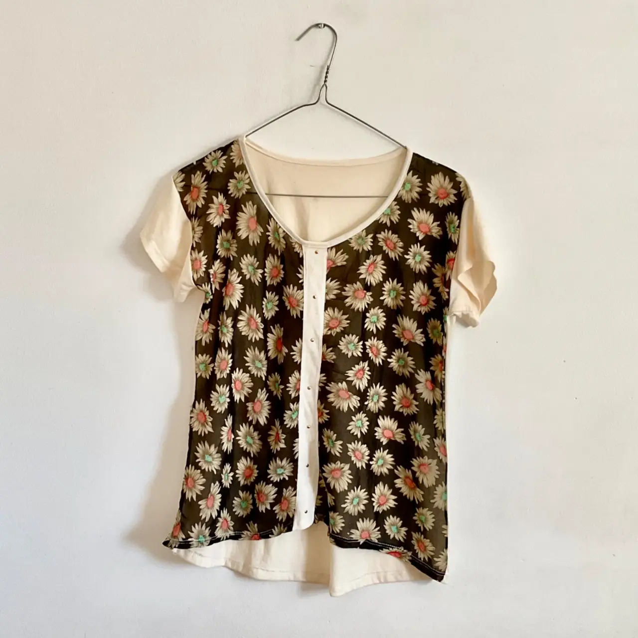 Blusa vintage con estampado floral en tonos marrones y blancos. Diseño con botones centrales y mangas cortas. Ideal para un look retro y femenino.