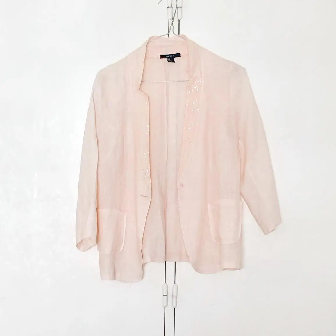 Blazer de mujer color rosa claro, con un botón y dos bolsillos delanteros. Detalles de brillos en la solapa. Ideal para un look elegante y sofisticado.