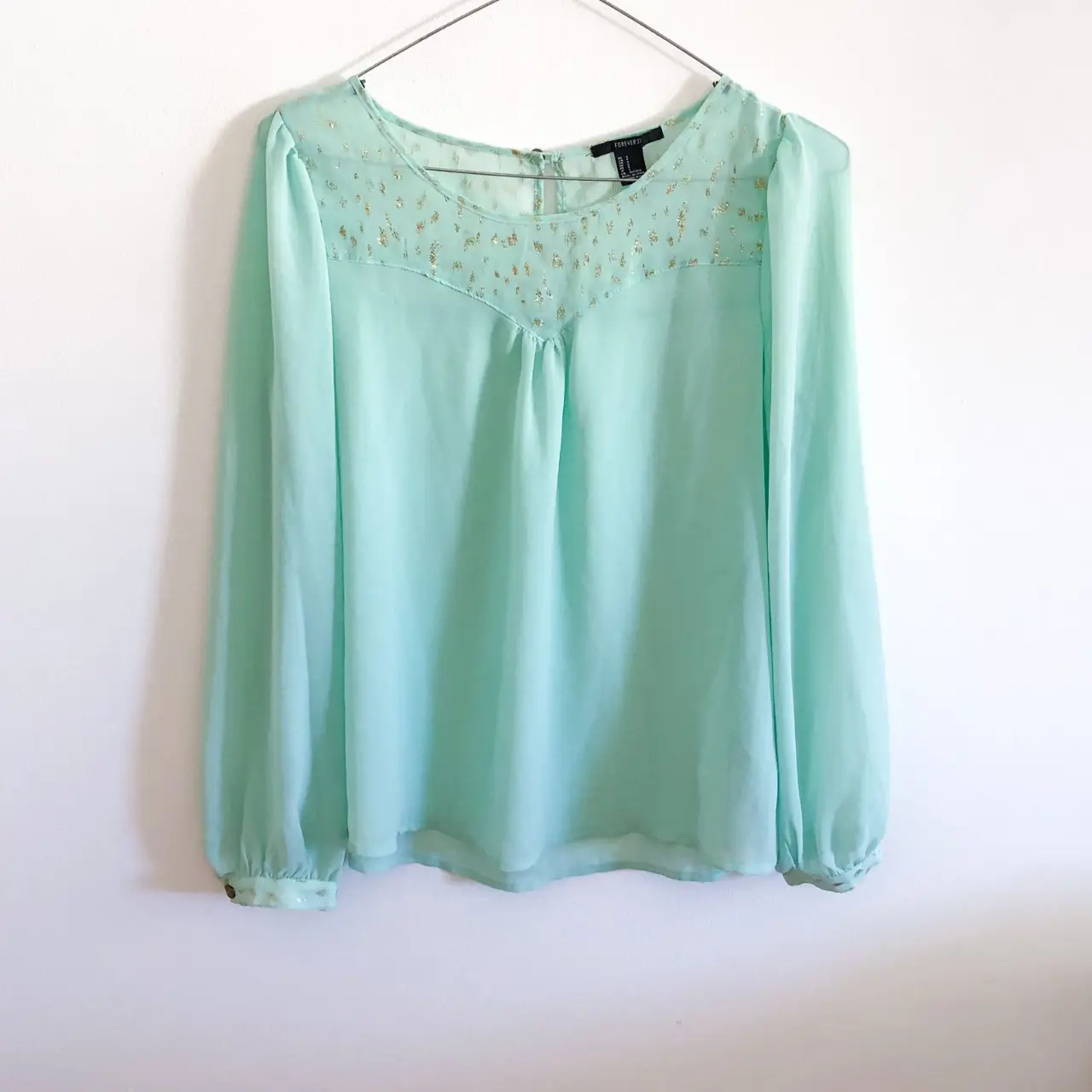 Blusa celeste de manga larga con detalles dorados en el pecho. Ideal para un look elegante y fresco.