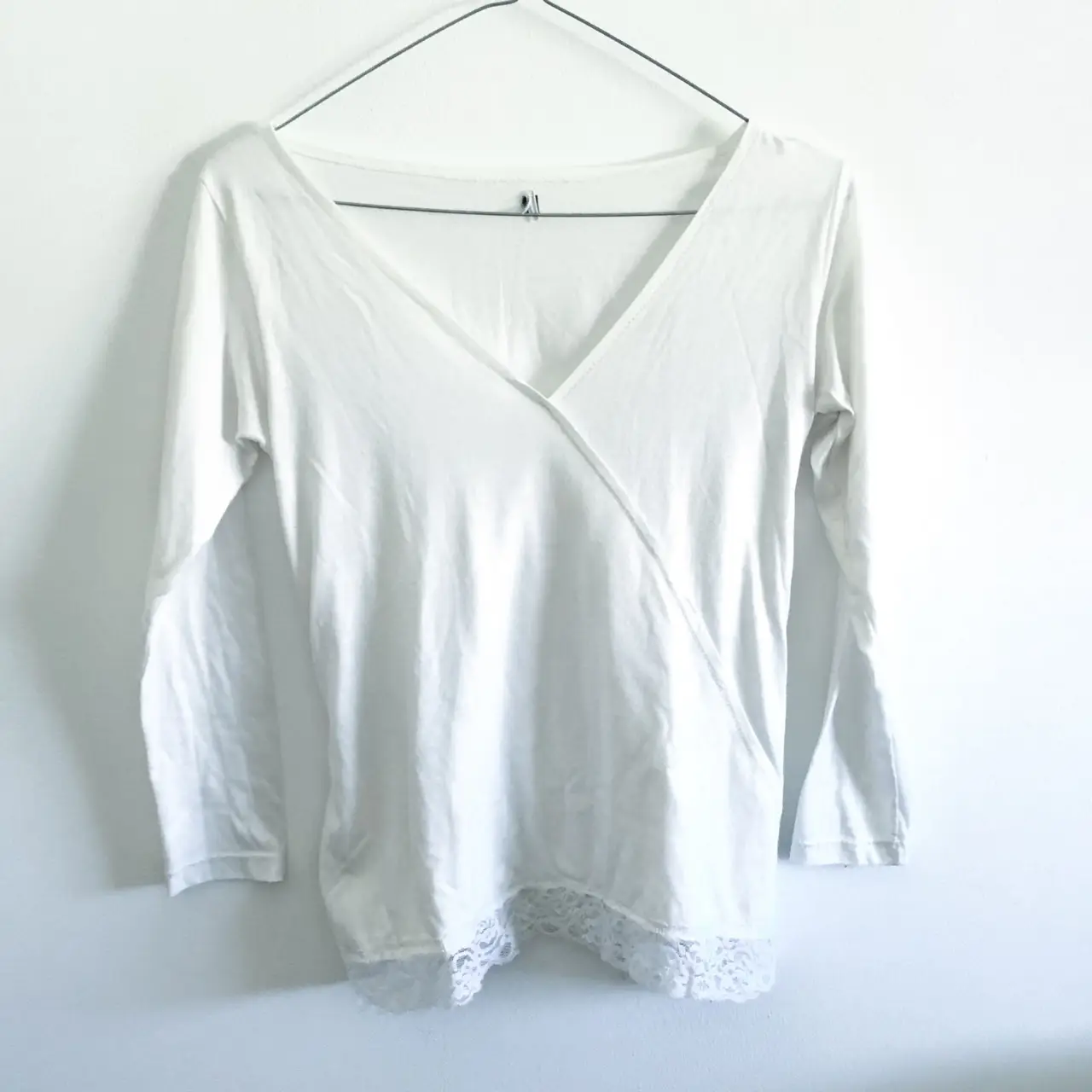 Blusa blanca de manga larga con escote en V cruzado y detalle de encaje en el bajo. Ideal para un look elegante y femenino.