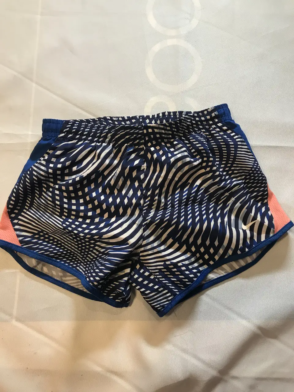 Short deportivo de mujer Nike, con estampado geométrico en tonos azul y blanco. Detalles en rosa y azul. Ideal para running y entrenamiento.