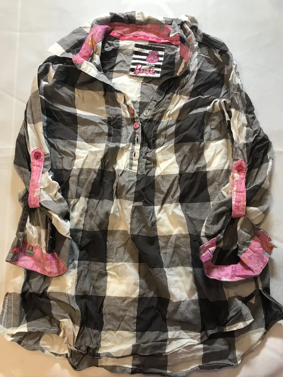 Camisa a cuadros en tonos grises y blancos con detalles en rosa. Manga larga con puños ajustables y cuello con detalles en rosa. Ideal para un look casual y moderno. Barbie talle 6
