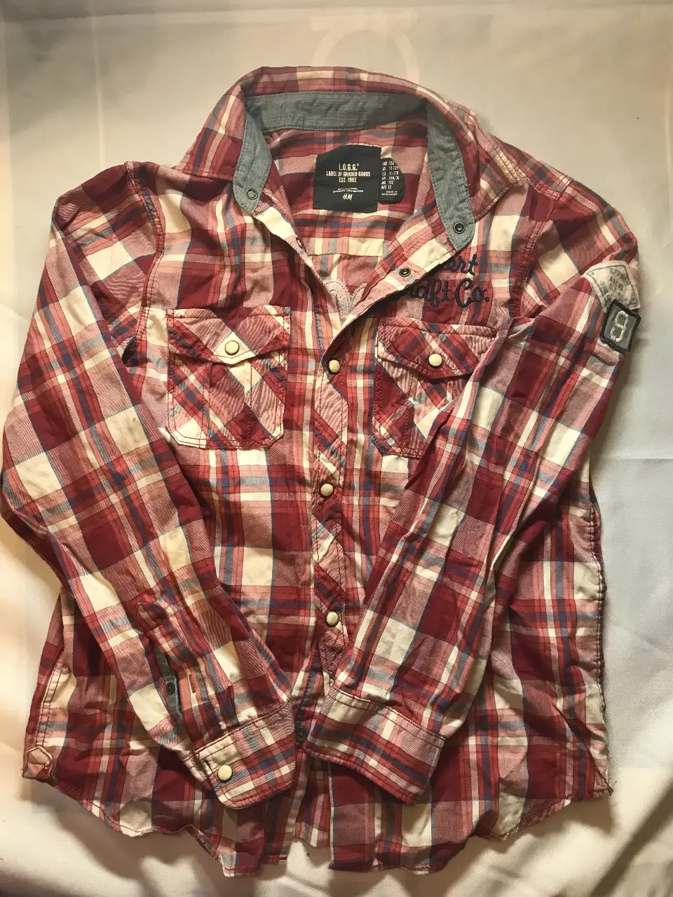 Camisa a cuadros roja y blanca de hombre, con detalles en azul y gris. Tiene dos bolsillos delanteros y un parche en la manga. Marca L.O.G.G. de H&M. 11/12 años