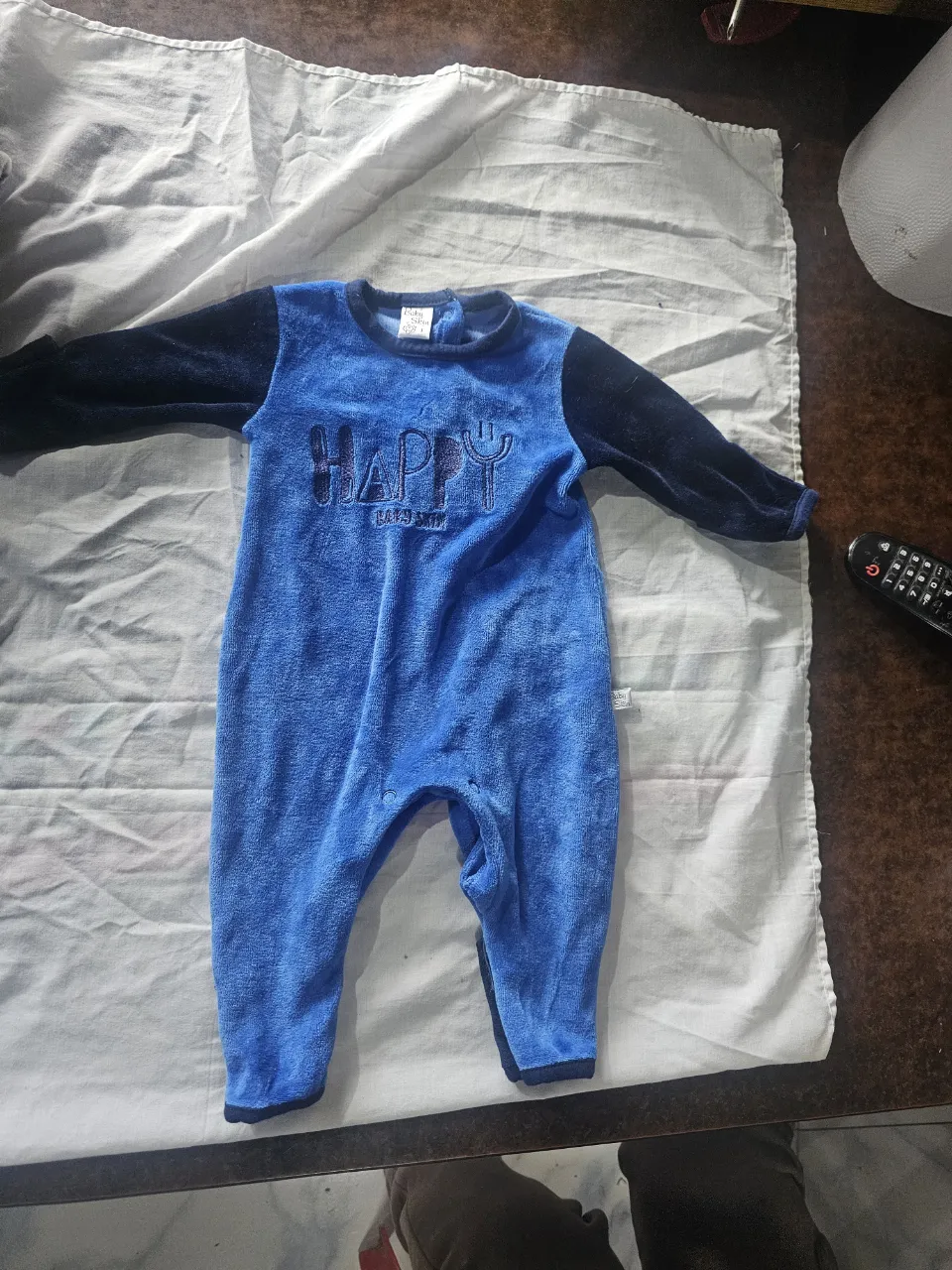 Body de bebé de plush azul con mangas negras. Tiene la palabra "HAPPY" bordada y un diseño de tenedor. Ideal para mantener a tu bebé abrigado y cómodo.