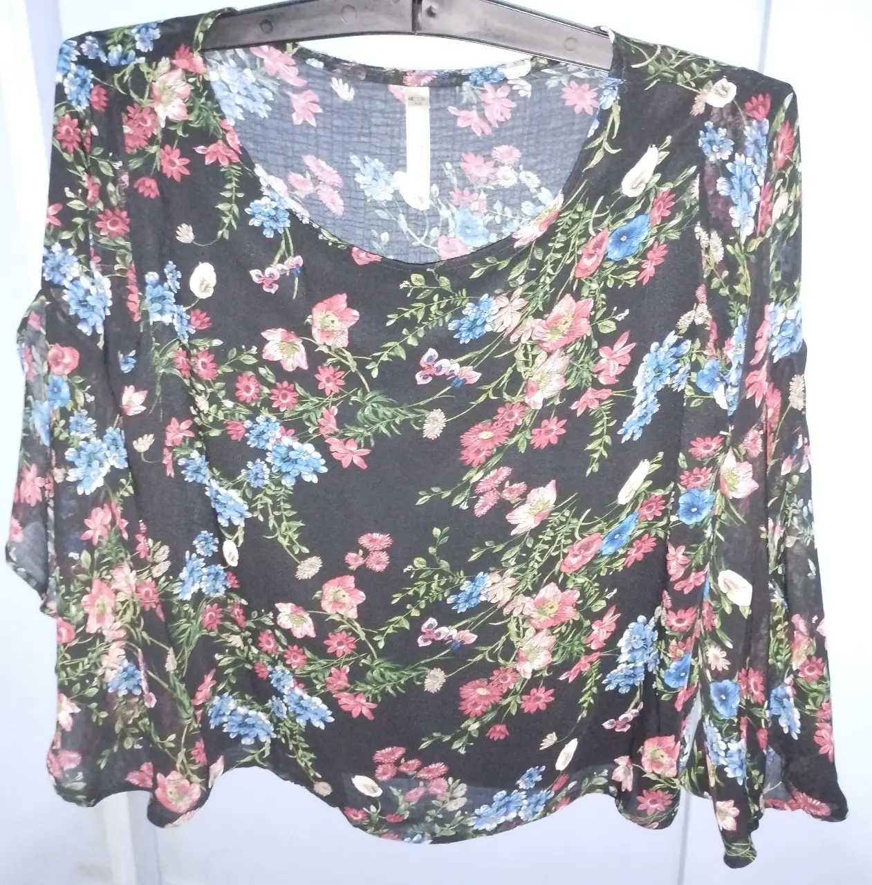 Blusa de mujer de gasa, con estampado floral en tonos rosa, azul y blanco sobre fondo negro. Diseño con mangas amplias con gajos y escote redondo amplio. Ideal para un look casual y fresco. Sisa 50 CM, largo total 50 CM, largo mangas 50 CM 
