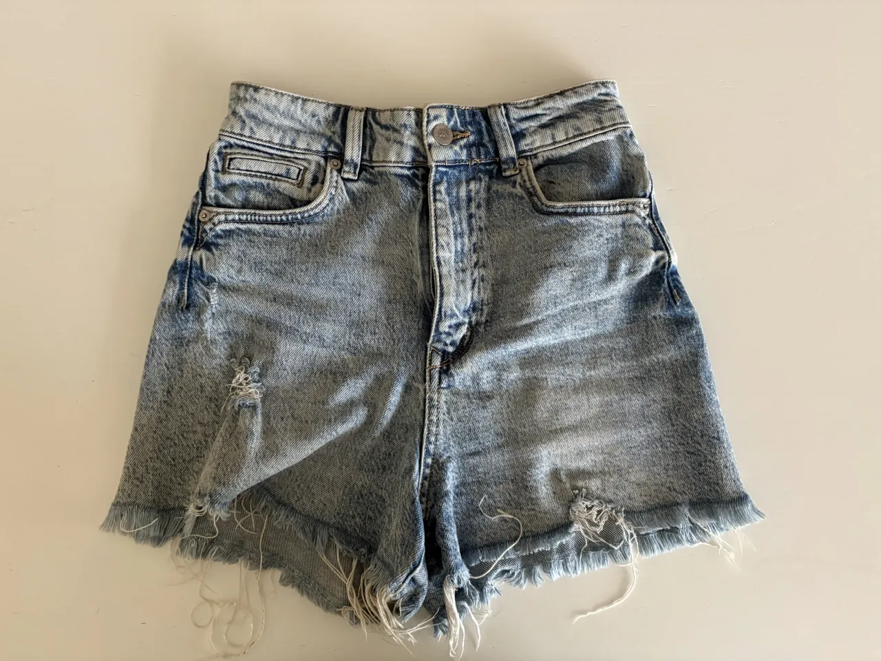Shorts de jean tiro alto con roturas y detalles desflecados en los bordes. Lavado tipo "stone washed" con desgastes.