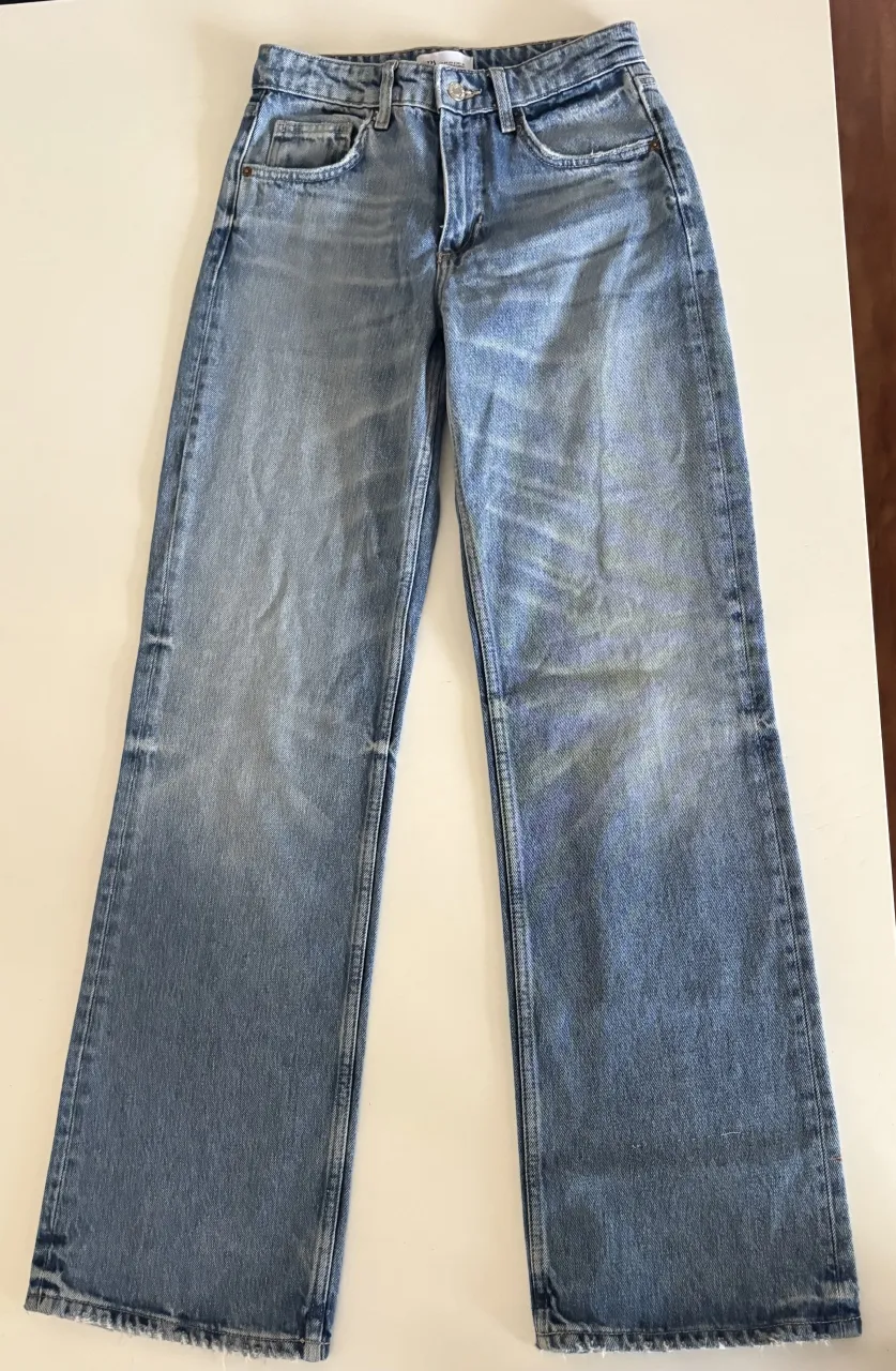 Jeans de denim azul con desgaste. Modelo de cinco bolsillos con cierre y botón.