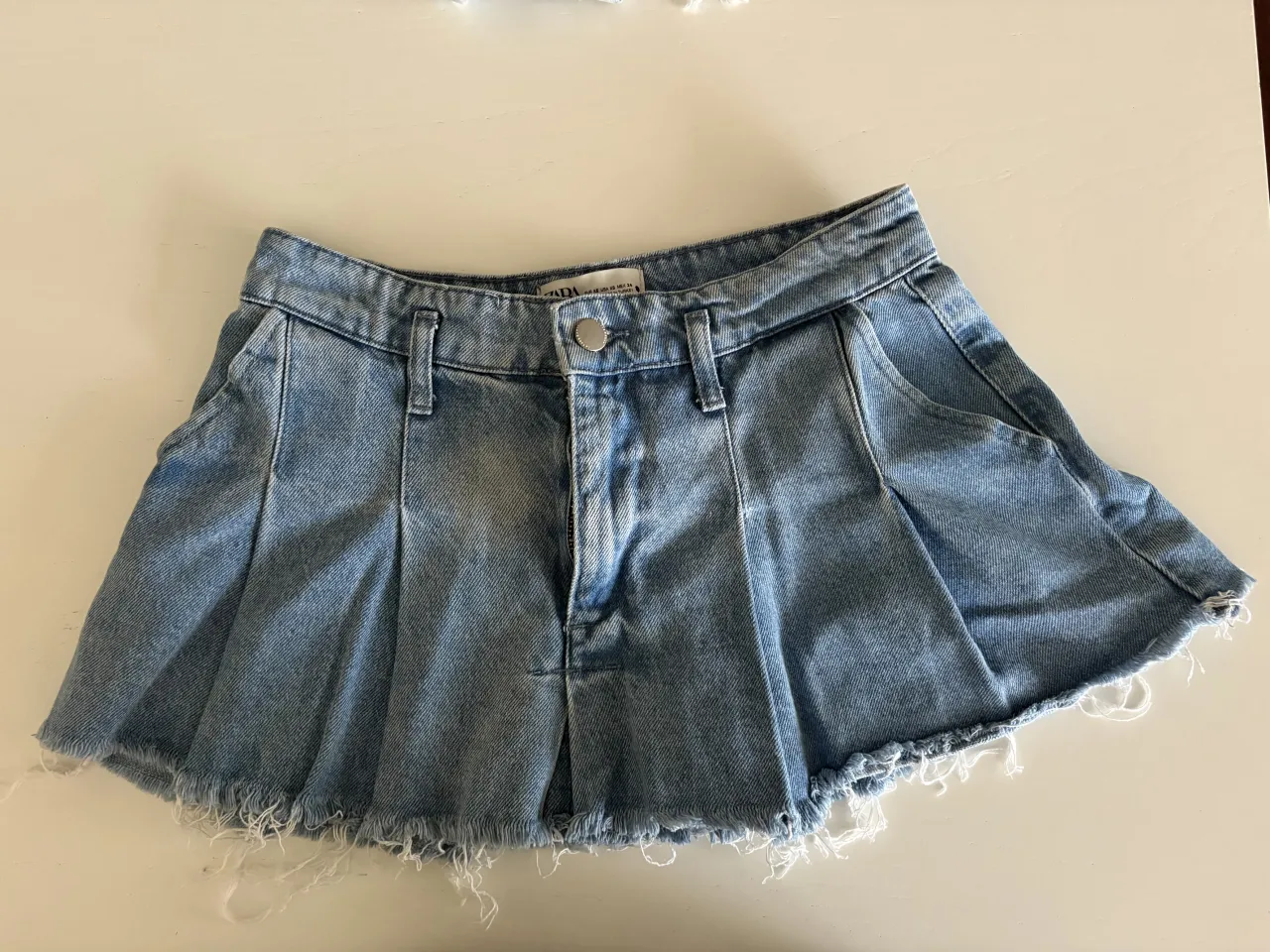 Pollera de jean tiro alto con tajos y terminación deshilachada.