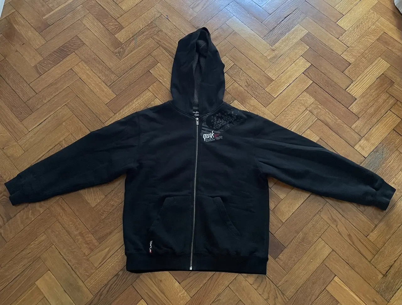 Buzo con cierre negro de la marca Quiksilver, con capucha y bolsillos delanteros. Ideal para un look casual y abrigado.