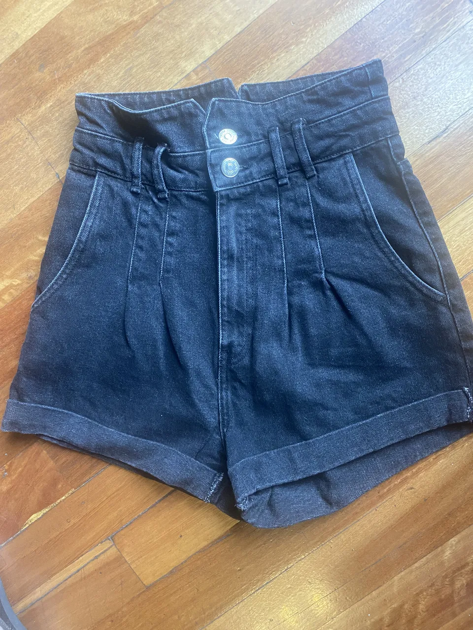 Shorts de jean negro tiro alto con doble botón y pinzas. Ideales para un look casual y moderno.