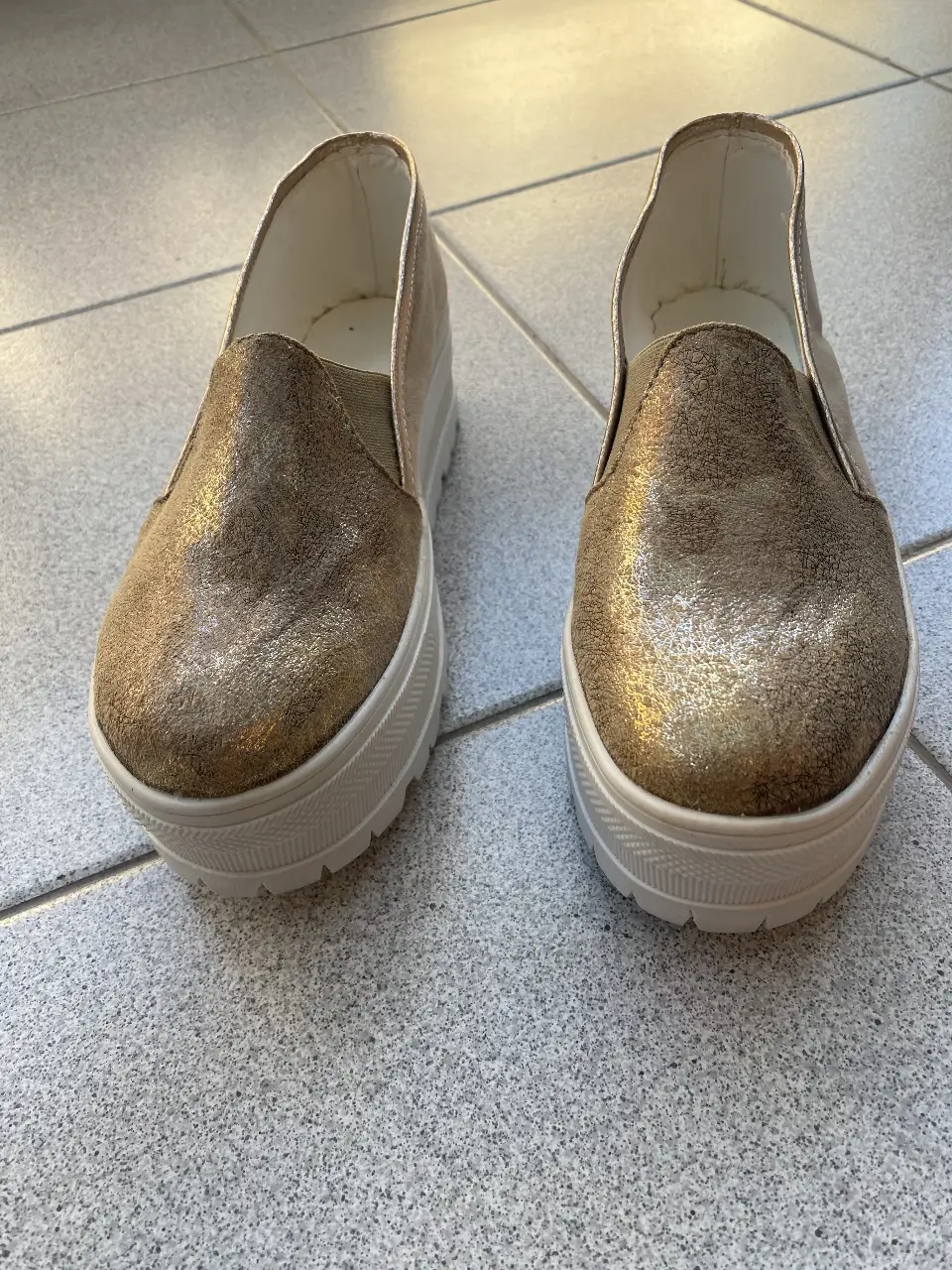 Zapatillas slip-on doradas con plataforma blanca. Ideales para un look casual y cómodo.