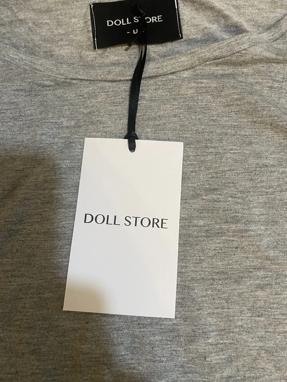 Remera de manga corta gris, con bolados de la marca DOLL STORE. Ideal para un look casual y cómodo.