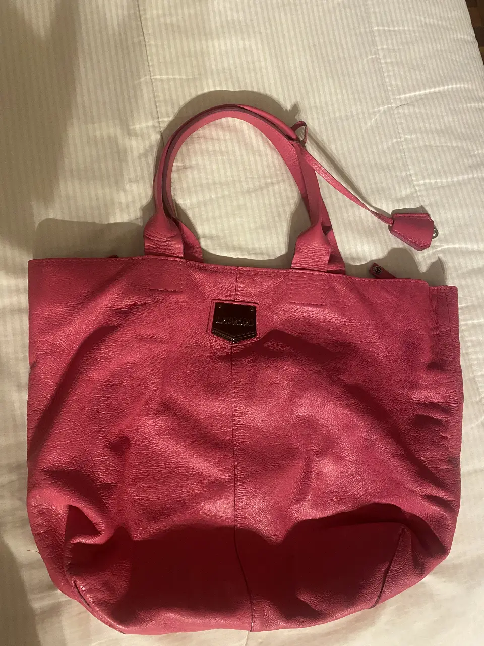 Cartera tote bag de cuero rosa, con detalle de placa metálica con el logo de la marca. Ideal para llevar todo lo necesario con estilo.