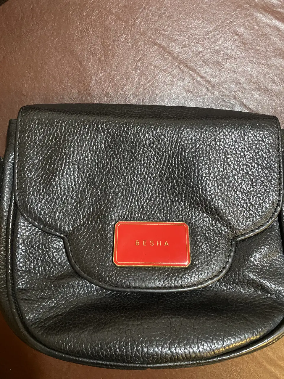 Cartera bandolera negra de cuero con detalle rojo y dorado. Ideal para llevar lo esencial con estilo.
