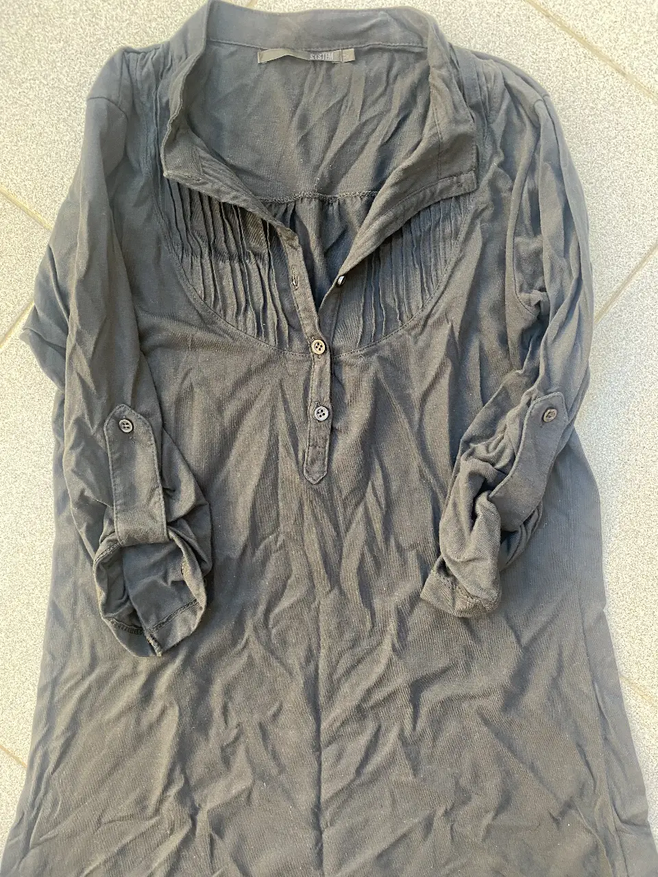 Blusa negra de manga larga con detalles plisados en el frente y botones. Ideal para un look casual y elegante.