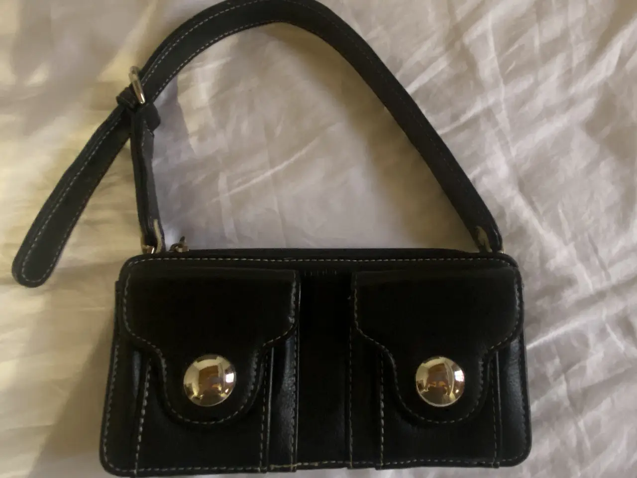 Cartera negra de mano, con dos bolsillos frontales con cierre de botón plateado. Marca Prüne.