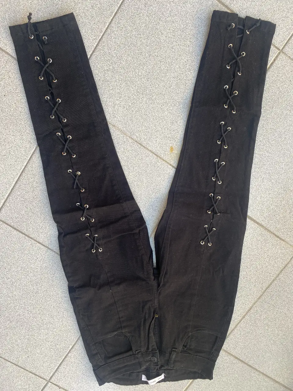 Pantalón de jean negro con detalles de cordones en los laterales. Corte recto, ideal para un look moderno y versátil.