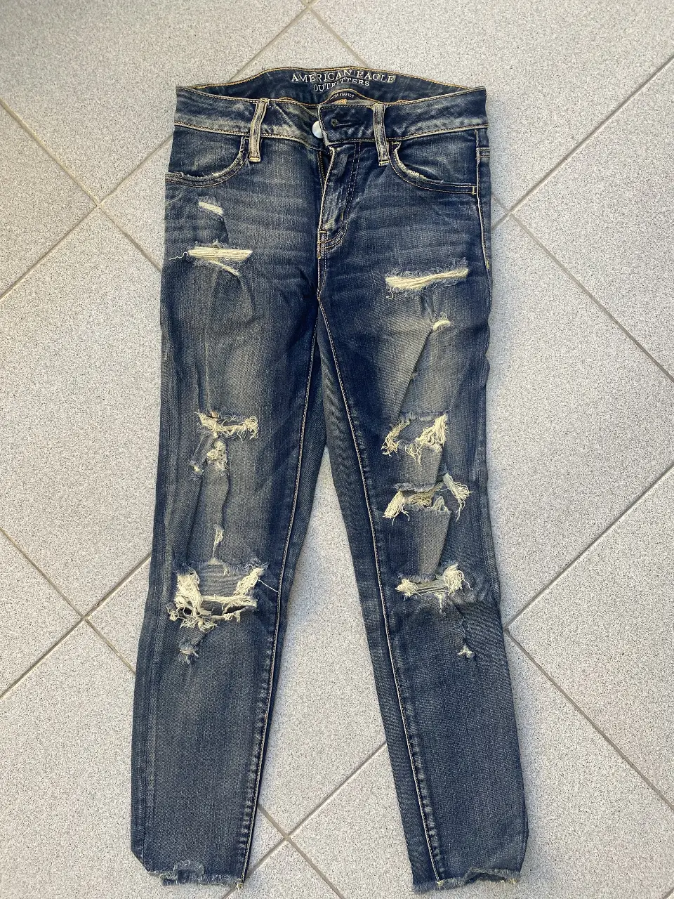 Jeans de mujer American Eagle, azul gastado con roturas en las rodillas y muslos. Tiro medio, ideal para un look casual, moderno y muy canchero.