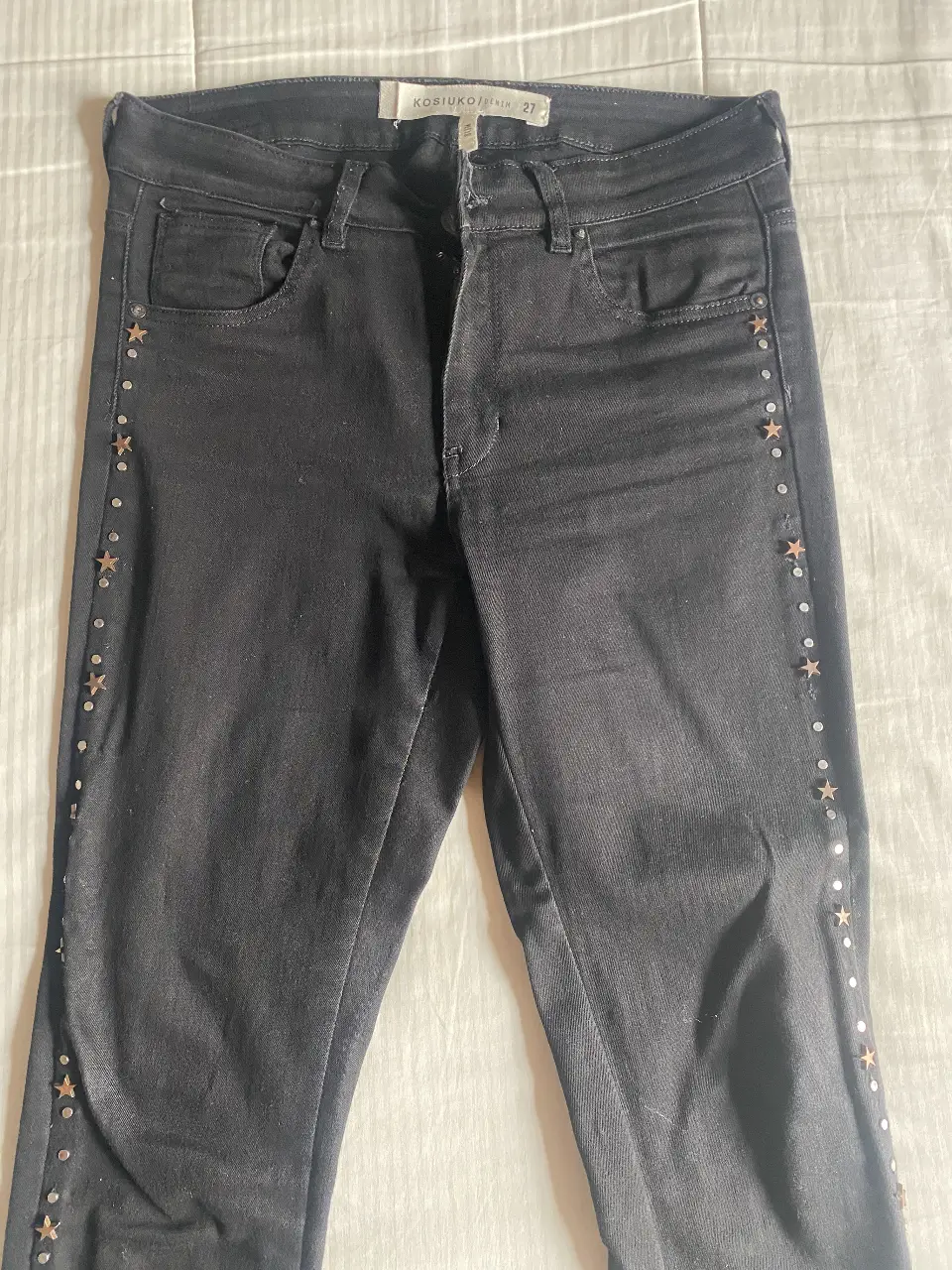 Jeans negro Kosiuko de mujer, tiro medio, con detalles de estrellas y tachas en los laterales. Talle 27, corte slim.