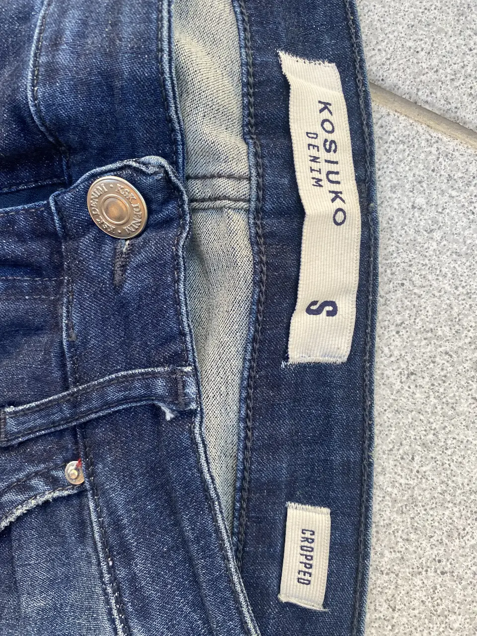 Jeans de mujer, de la marca Kosuko, color azul oscuro, con detalles de desgaste y roturas. Talle S, corte cropped con cierre en los tobillos.