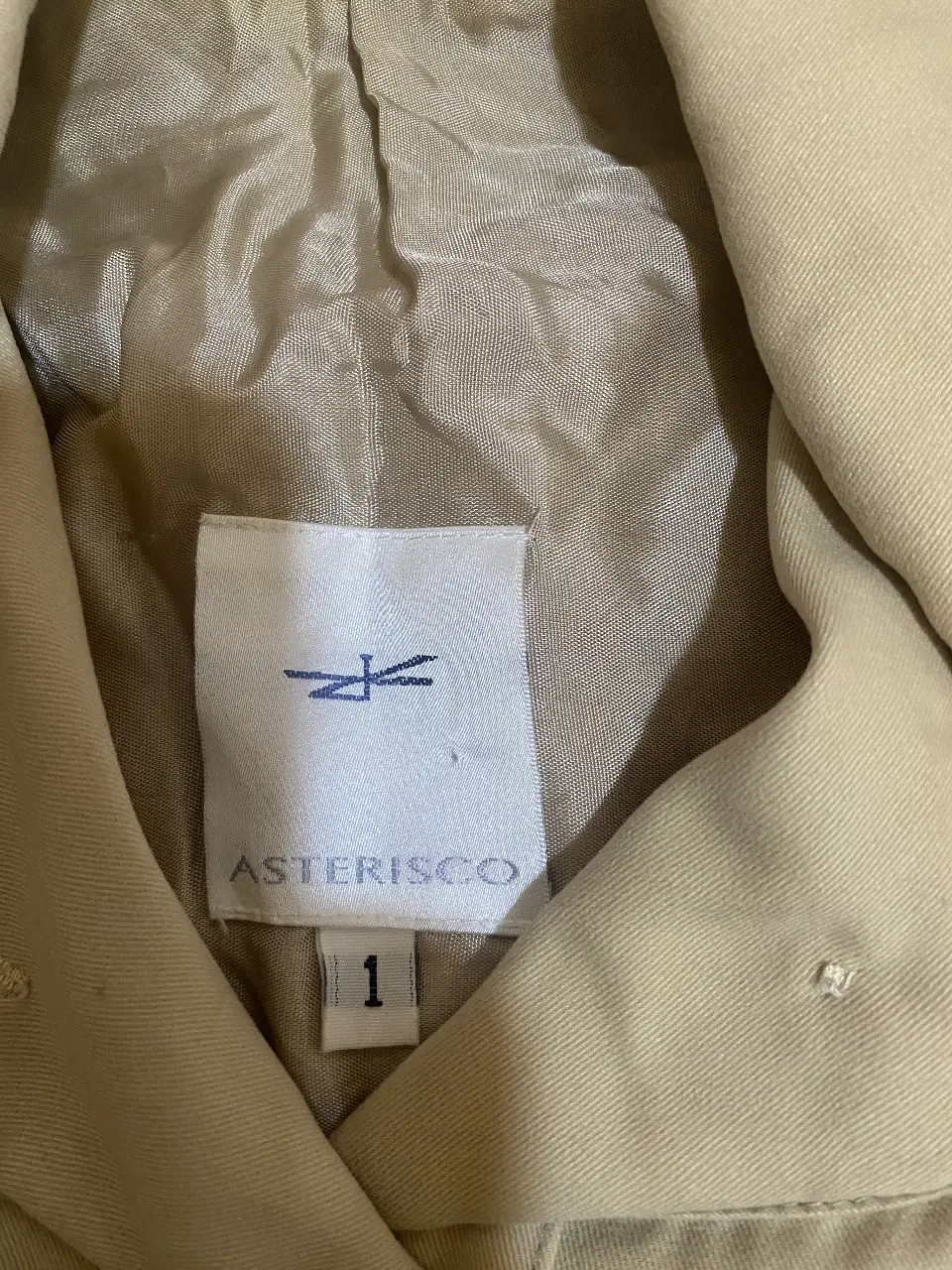 Trench Asterisco color crudo, con cinturón y botones dorados. Ideal para un look elegante y sofisticado.