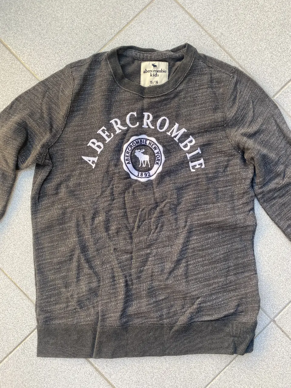 Buzo de cuello redondo Abercrombie Kids, gris jaspeado, con logo bordado en el frente. Talle 15/16.