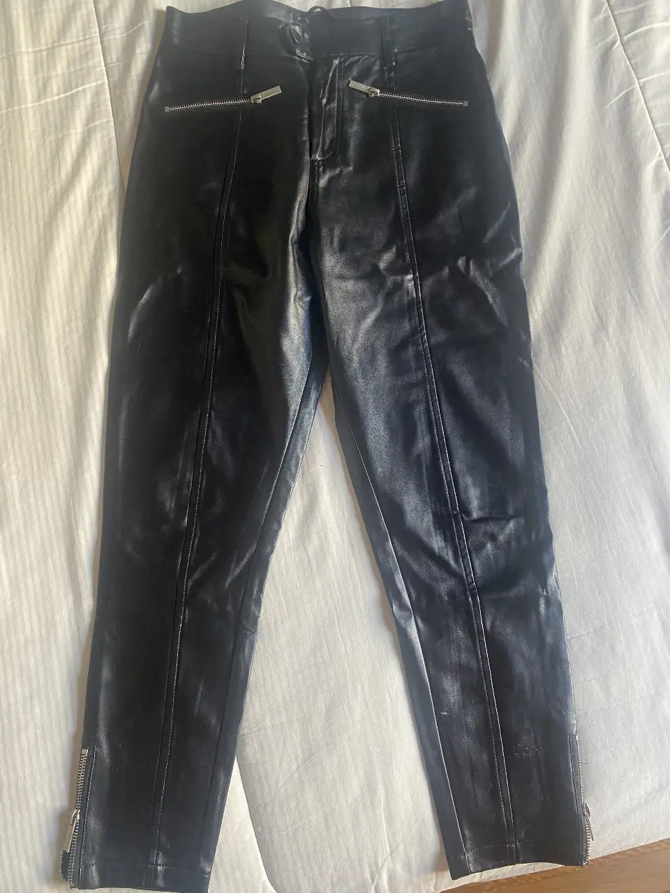 Pantalón de vestir negro de cuero sintético con cierre y detalles metálicos. Ideal para un look elegante y moderno.