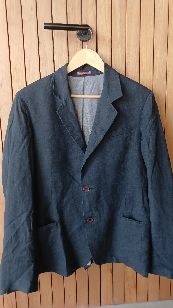 Blazer de tela color gris oscuro con tres botones al frente. Posee bolsillos laterales y en el pecho. Los puños tienen cuatro botones.