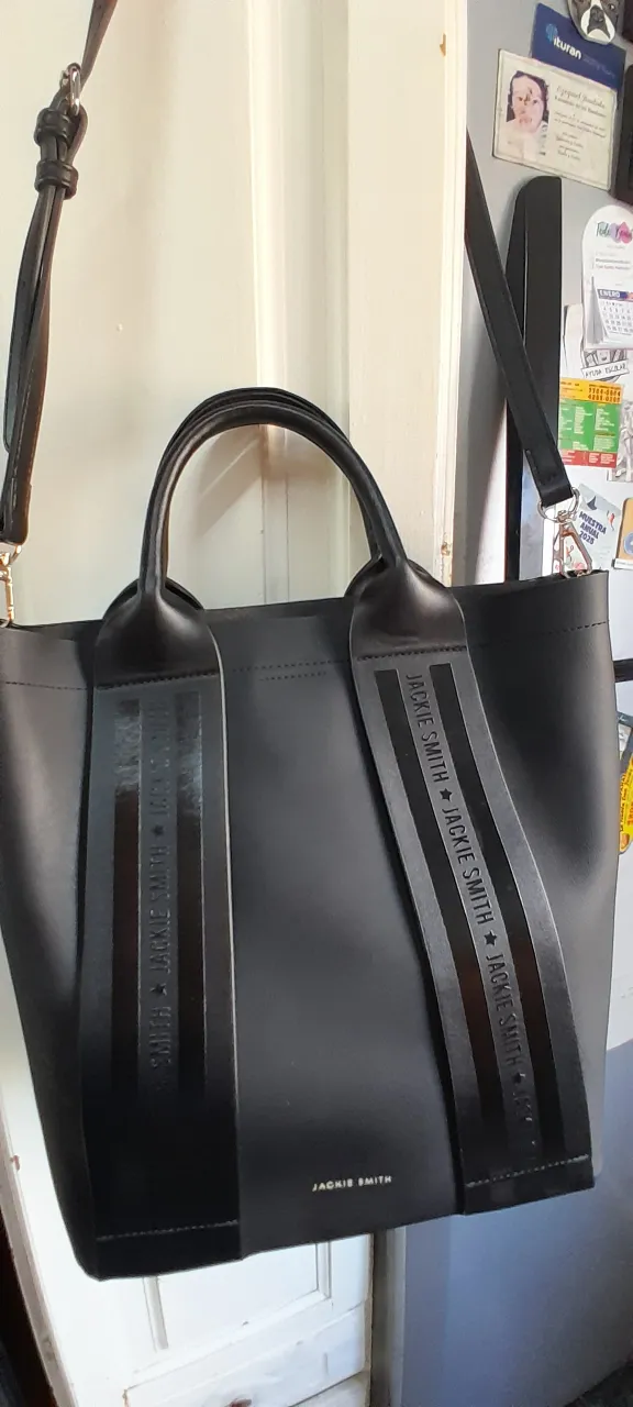 Bolso negro de cuero, con tiras estampadas con el logo de la marca. Tiene dos asas cortas y una correa larga desmontable. Ideal para el día a día.