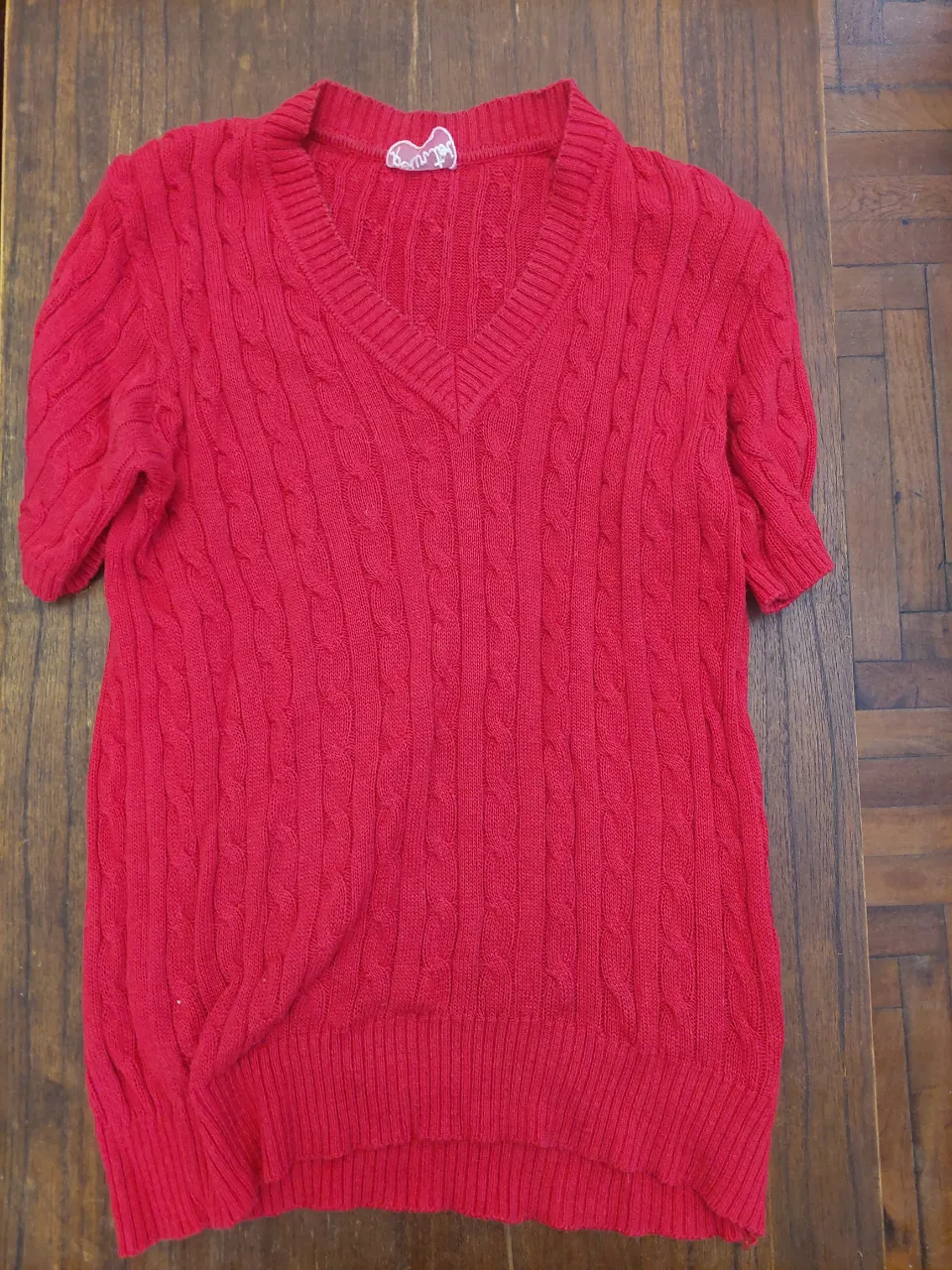Sweater rojo de tejido trenzado con escote en V y mangas cortas. 