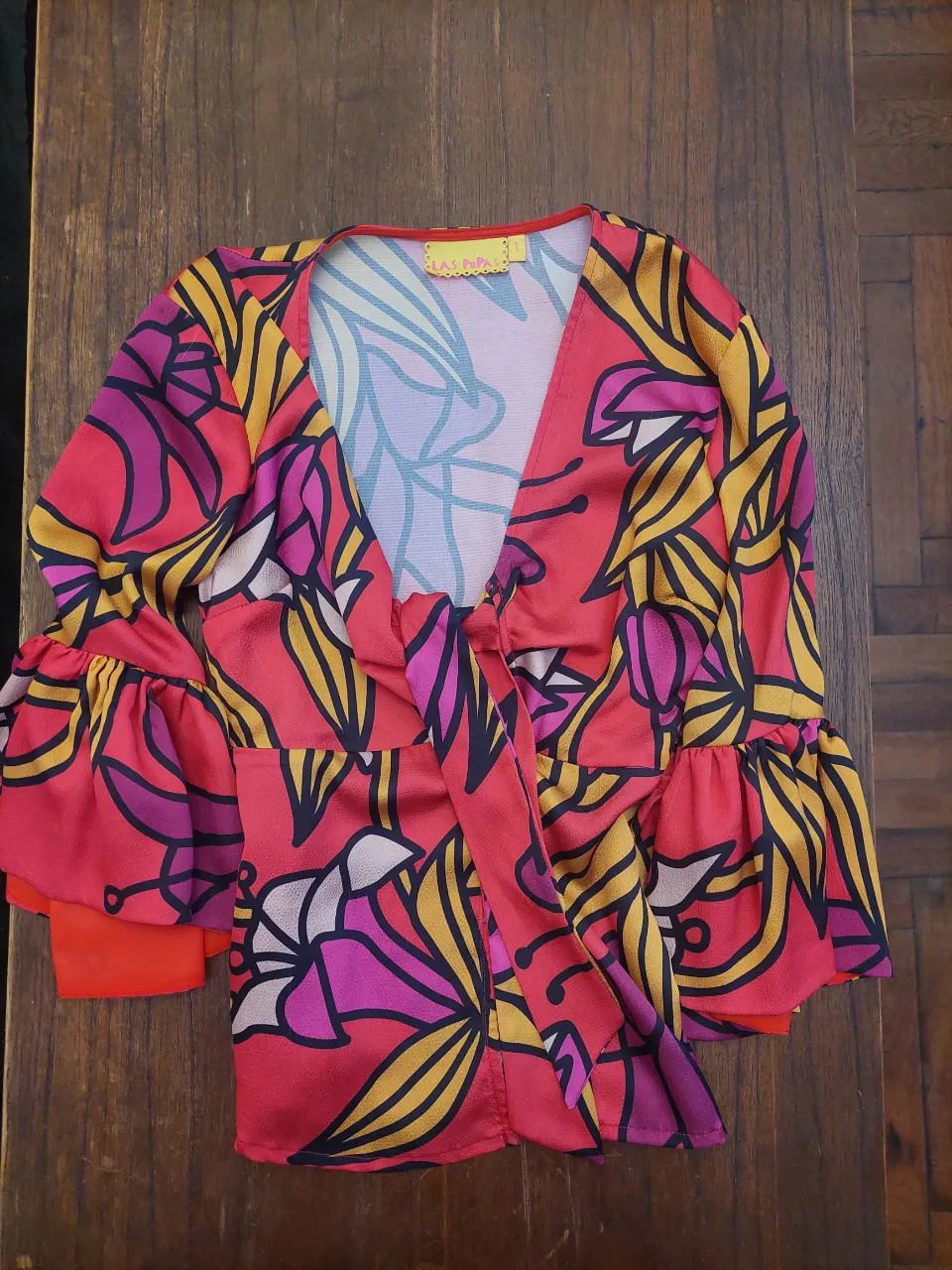 Blusa súper linda y colorida con estampado floral vibrante. Tiene mangas largas con volados y un lazo en la parte delantera que le da un toque chic. Ideal para un look canchero y alegre.