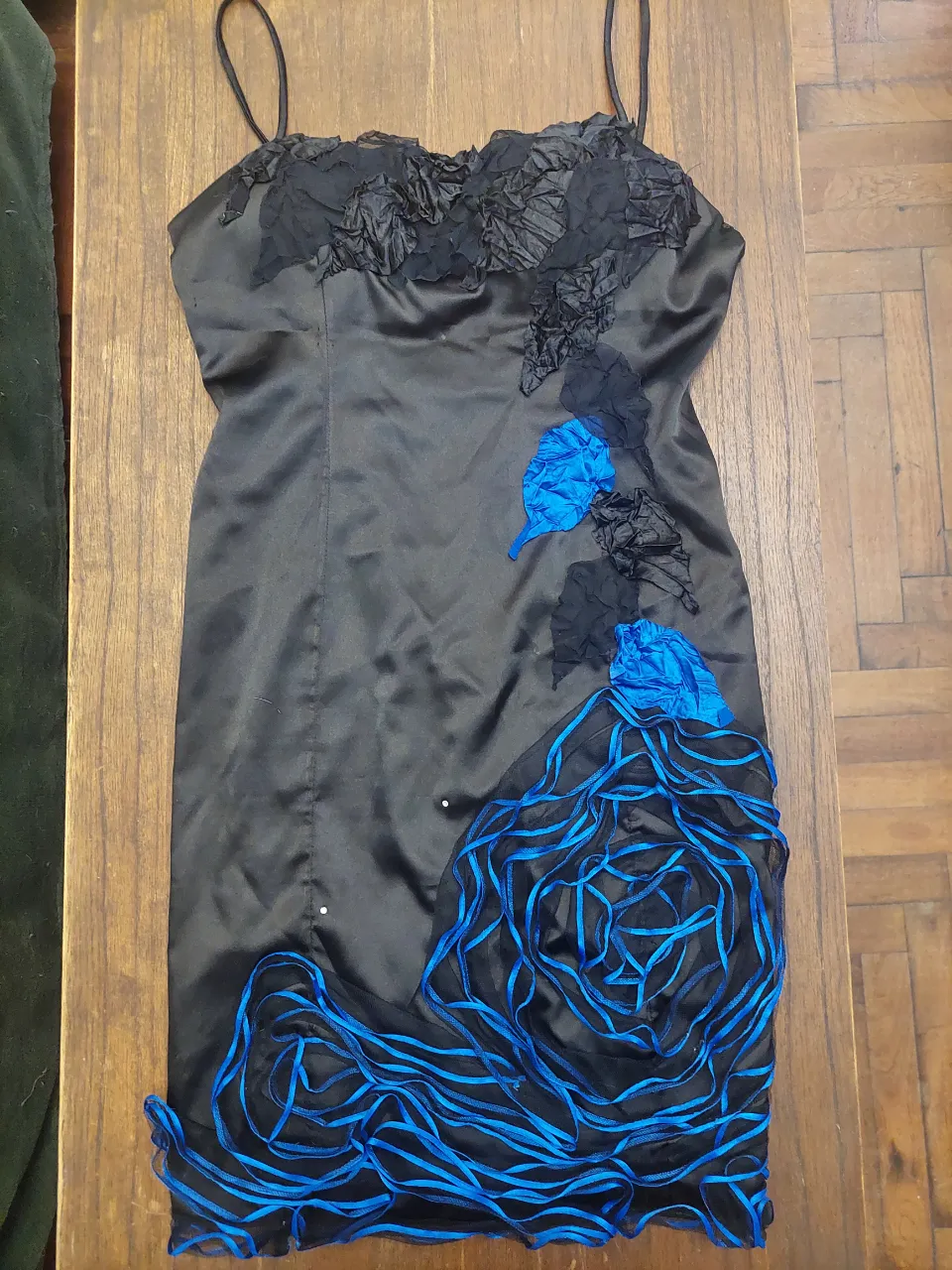 Vestido negro corto con tiras finas y detalles de flores en relieve y cintas azules. Ideal para una noche especial o una fiesta.