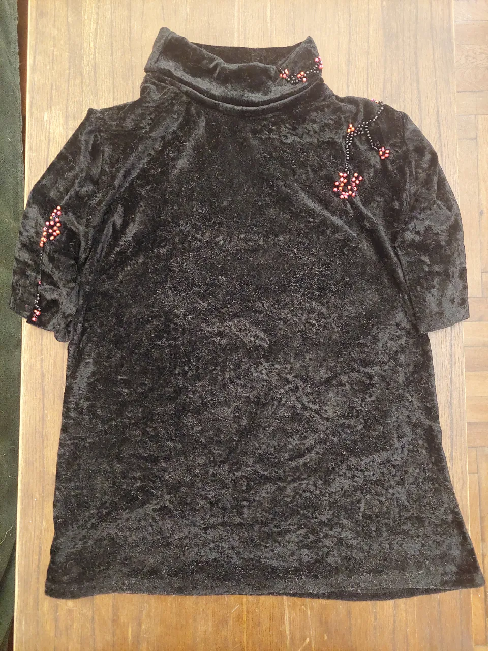 Remera negra de terciopelo con cuello alto y detalles de mostacillas rojas y negras en el cuello y mangas. Un diseño único y elegante, perfecto para lucir en una salida o fiesta.